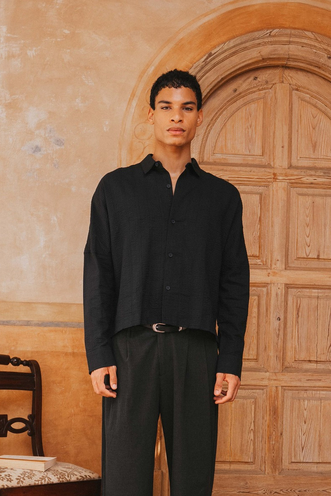 Man wearing a black shirt and pants standing in front of a wooden door.