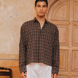 Man wearing a plaid shirt and white pants standing in front of a wooden door.