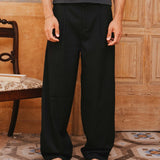 Person wearing black pants and a gray tank top standing in a room with wooden paneling and patterned floor.